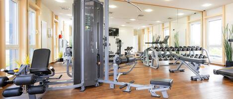 Un gimnasio con diversos equipos de ejercicio, incluyendo una jaula para sentadillas, mancuernas y máquinas de cardio.