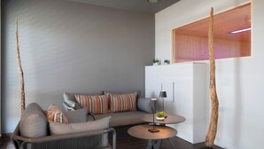 A modern living room with a grey sofa, striped pillows, a small round table with a lamp, and a wooden accent wall. - Best Western Plus Hotel Köln City (Cologne)