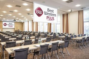A conference room with rows of tables and chairs, a large banner with 'Best Western PLUS' branding, and a projector screen in the background. - Best Western Plus Hotel Köln City (Cologne)