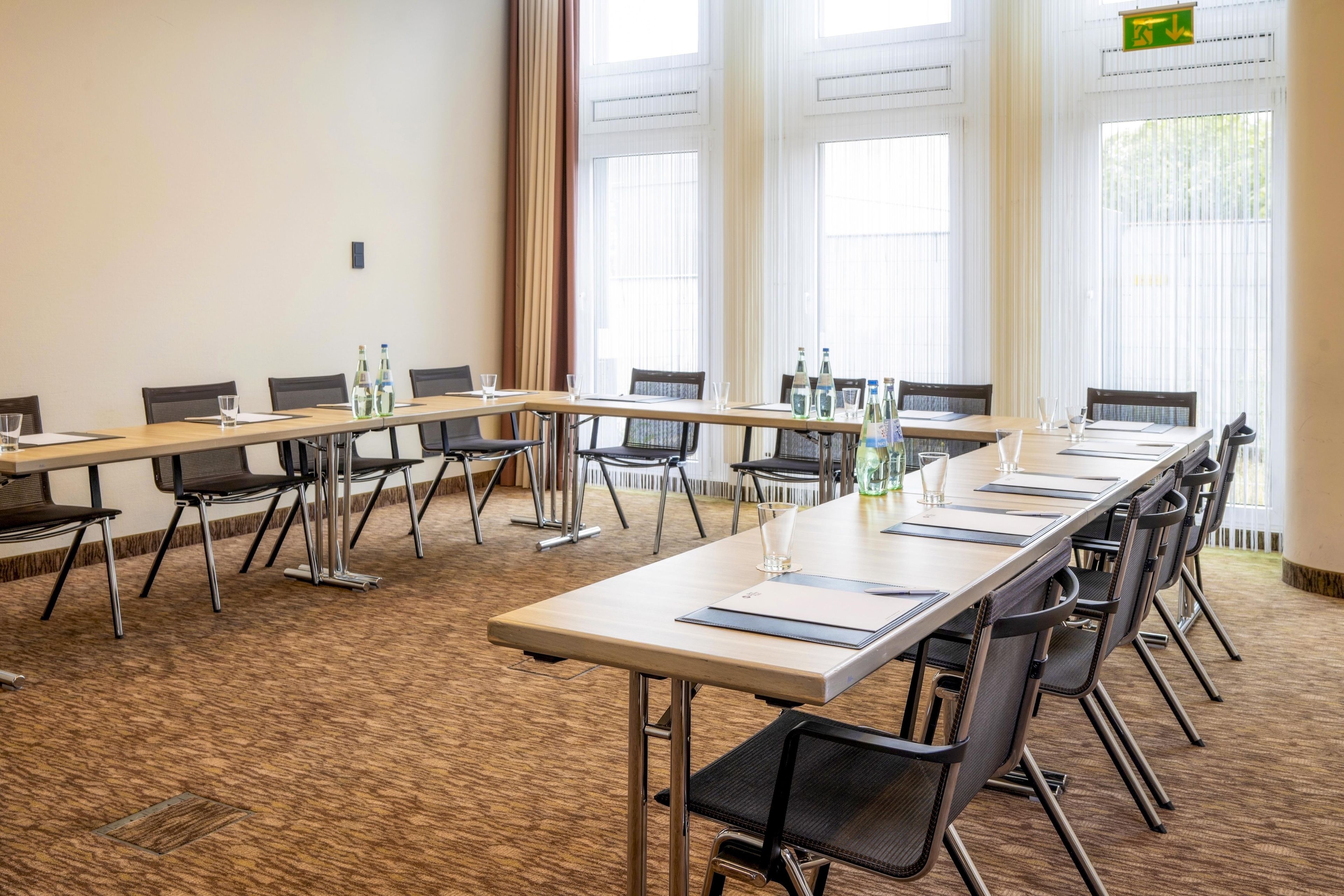 Ein Konferenzraum mit mehreren Tischen und Stühlen, großen Fenstern und einem Teppichboden.