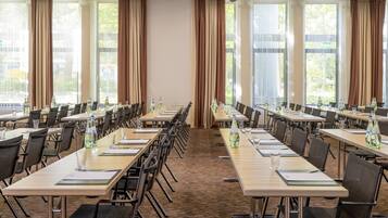 Une salle de conférence dotée de plusieurs tables et chaises, de grandes fenêtres avec des rideaux et d’un sol recouvert de moquette.
