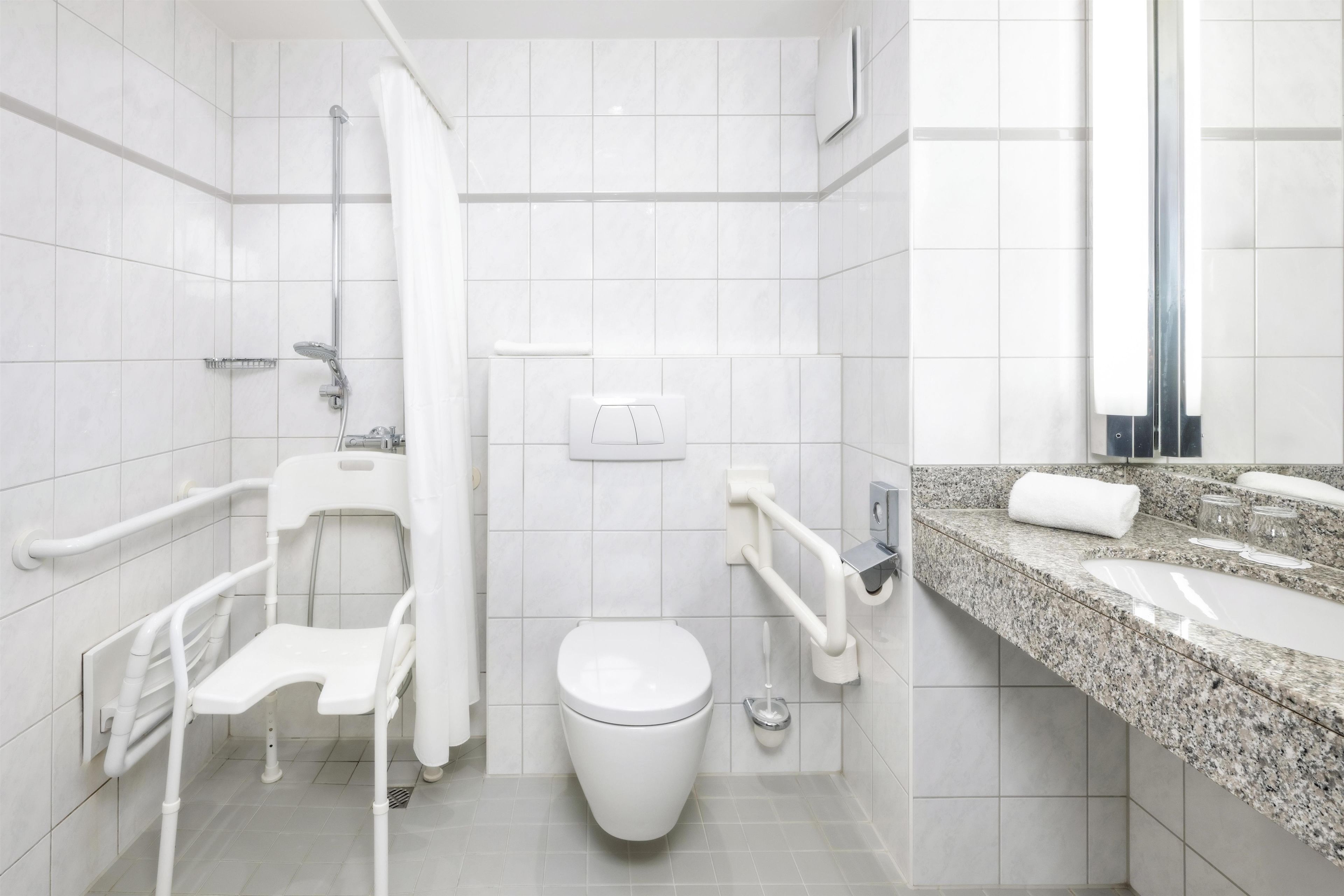 Ein modernes Badezimmer mit Toilette, Haltegriffen, Dusche und Waschbecken mit Marmorplatte.