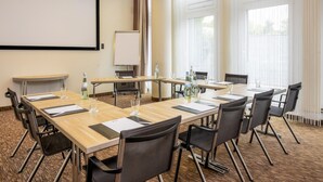 A conference room with a large screen, multiple tables, chairs, and a projector. - Best Western Plus Hotel Köln City (Cologne)
