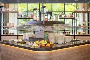 A buffet setup with a glass display case, a variety of fruits, and stacked plates. - Best Western Plus Hotel Köln City (Cologne)