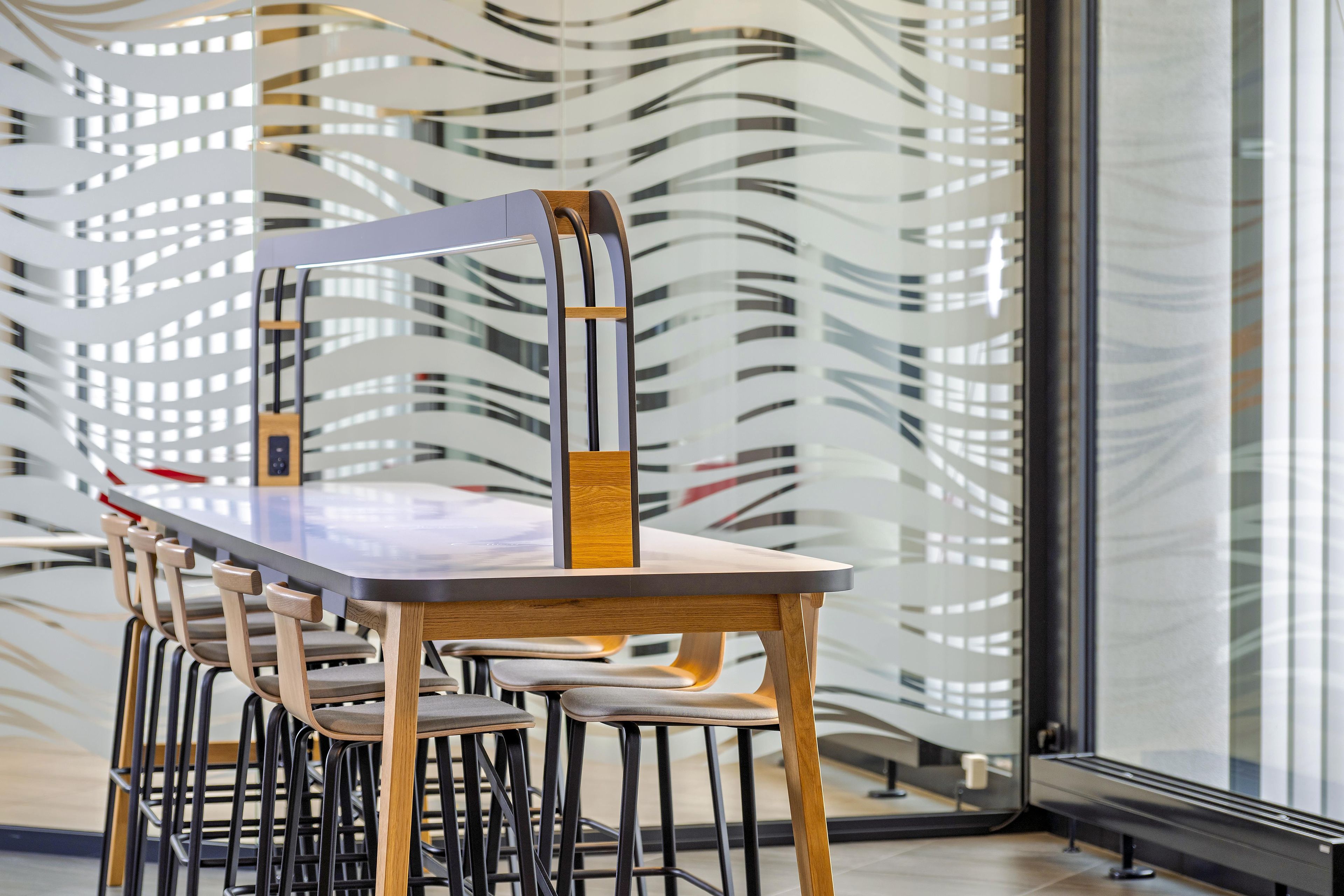 A modern dining area with a long table and chairs, a decorative wall, and a large window.