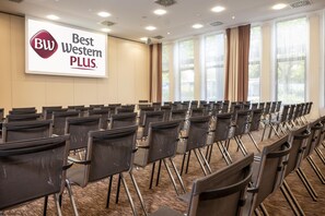 A conference room with rows of chairs, a large screen displaying 'Best Western PLUS' logo, and large windows with curtains. - Best Western Plus Hotel Köln City (Cologne)