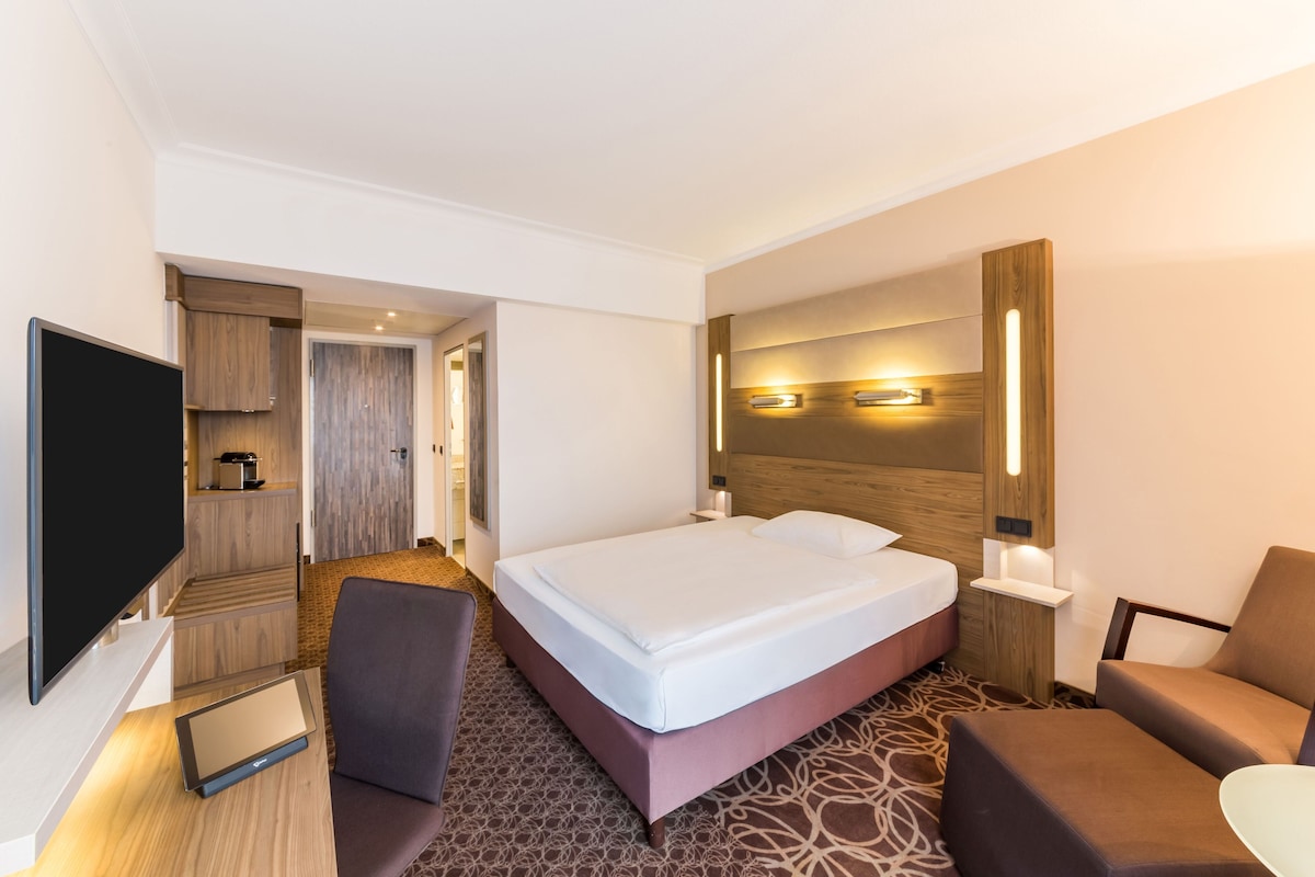 A hotel room with a large bed, a TV, a desk, and a seating area.