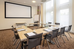 A conference room with a large screen, multiple tables, and chairs. - Best Western Plus Hotel Köln City (Cologne)
