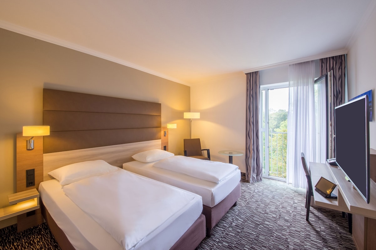 A hotel room with two beds, a desk with a computer, a TV, and a window with curtains.