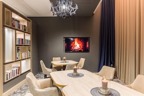 A hotel room with a fireplace, a bookshelf, a dining table with chairs, and a chandelier. - Best Western Plus Hotel Köln City (Cologne)