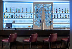 A bar area with multiple shelves of liquor bottles, a decorative partition, and bar stools. - Best Western Plus Hotel Köln City (Cologne)