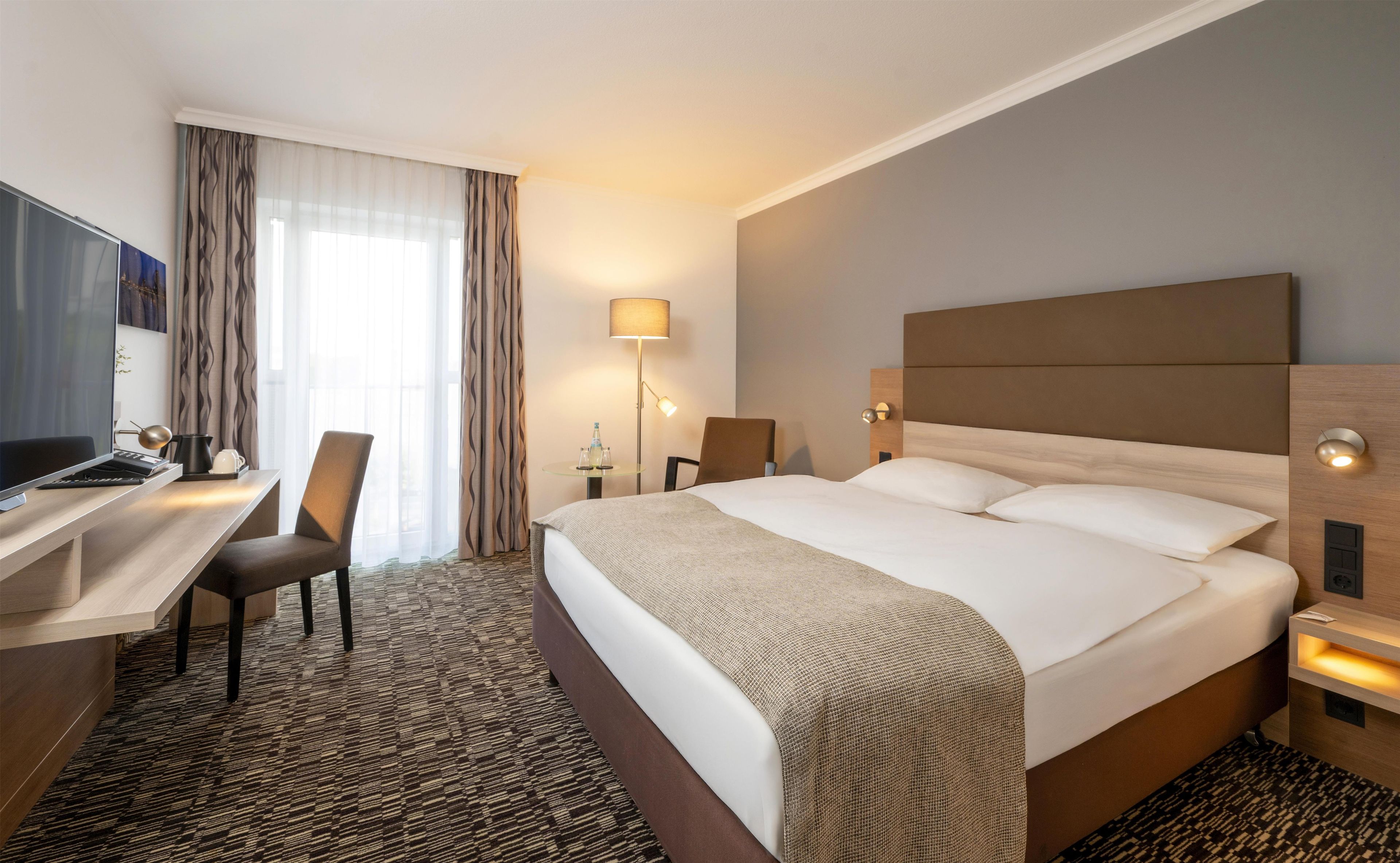 Una habitación de hotel con cama, escritorio, silla, lámpara y televisor.