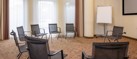 Un salón de conferencias con seis sillas de malla negra dispuestas en semicírculo, una pizarra y una pantalla de proyector en la pared.