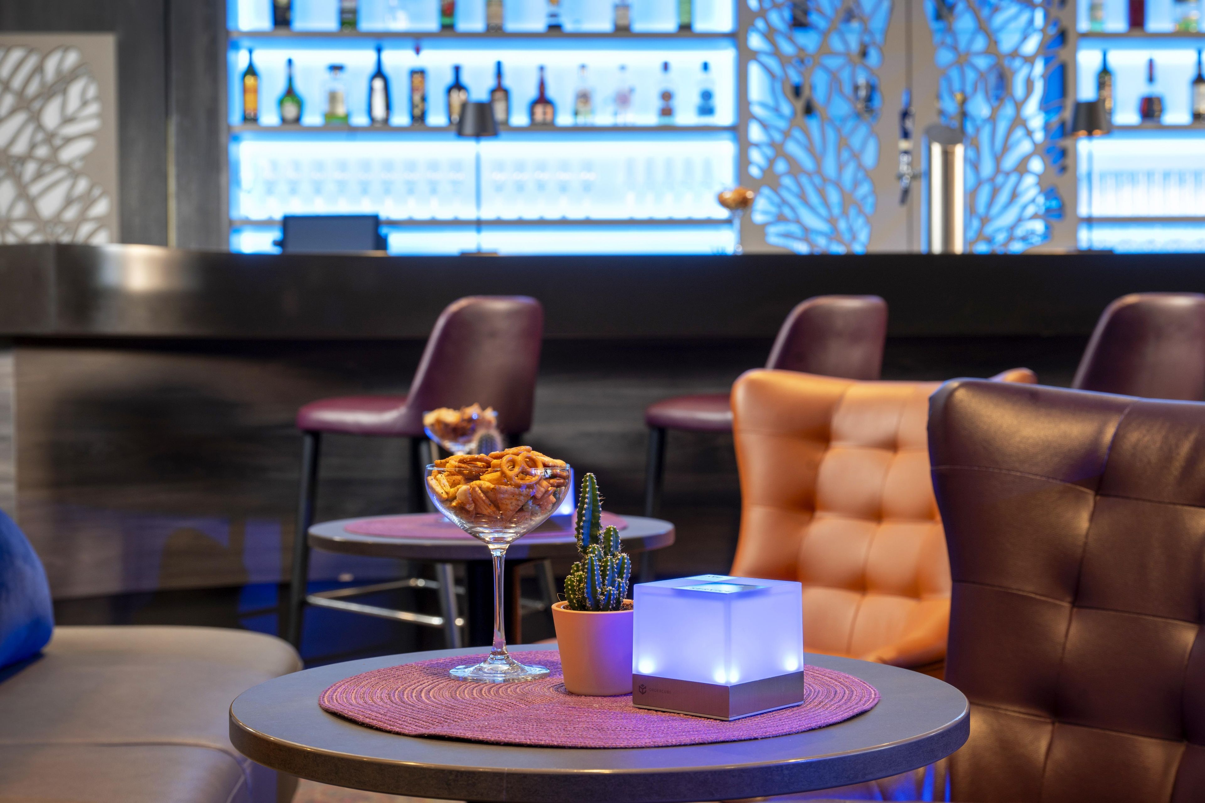 A bar area with leather seating, a glass dessert bowl, a cactus plant, and a lit box on a table.