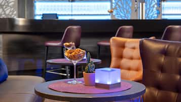 A bar area with leather seating, a glass dessert bowl, a cactus plant, and a lit box on a table.