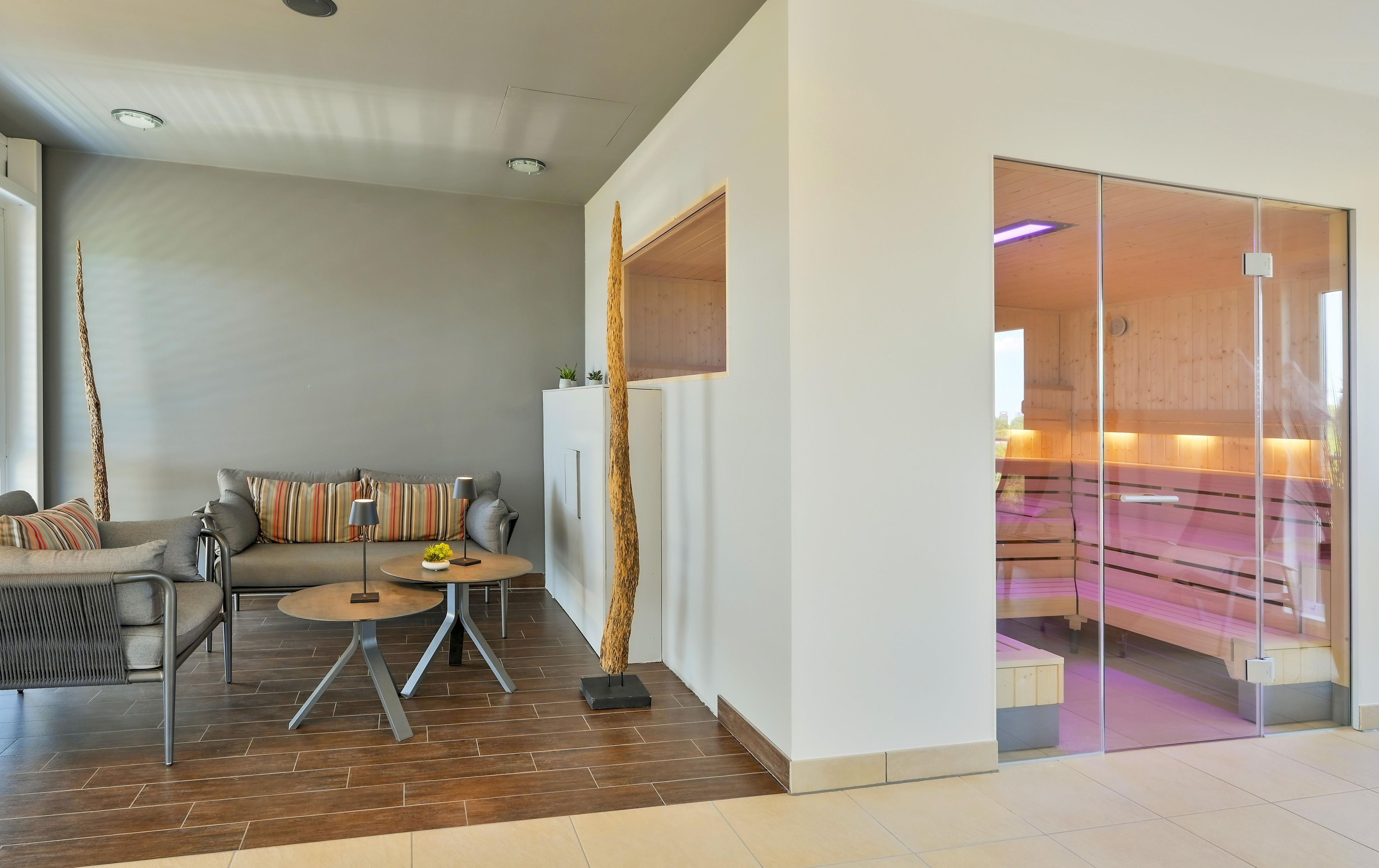 A modern living room with a sofa, two side tables, and a glass partition leading to a sauna area.