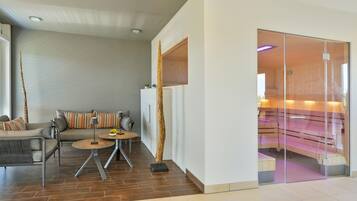 A modern living room with a sofa, two side tables, and a glass partition leading to a sauna area.