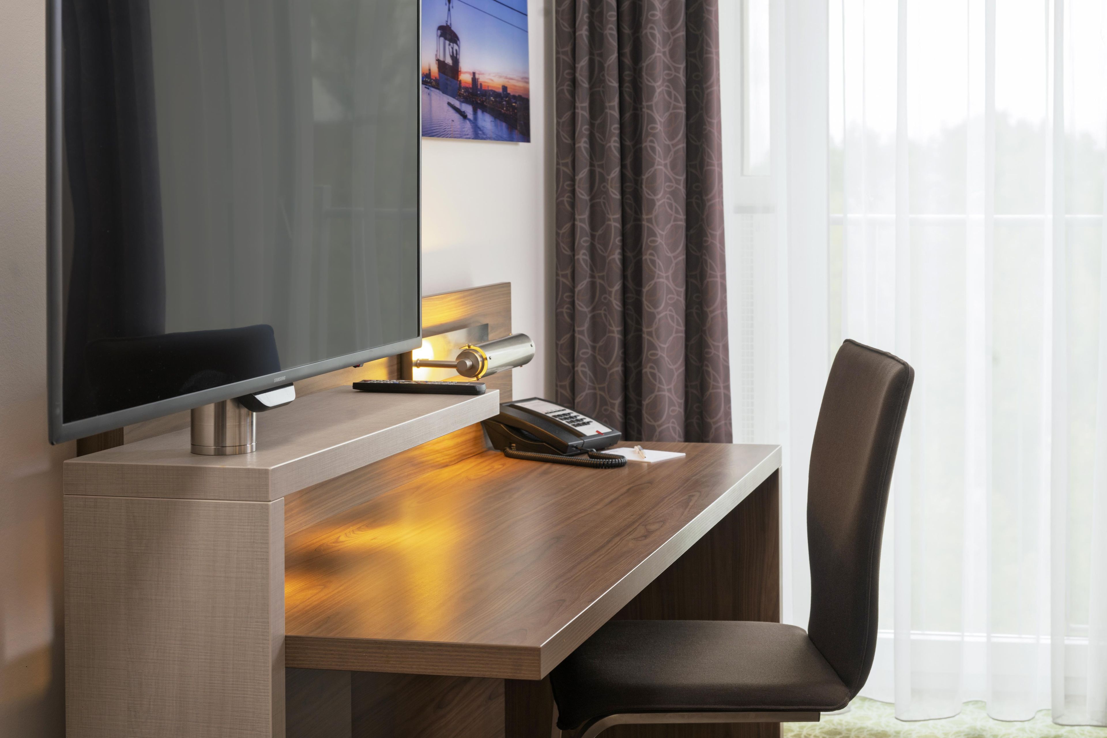 A hotel room with a desk, a chair, a television, and a telephone.