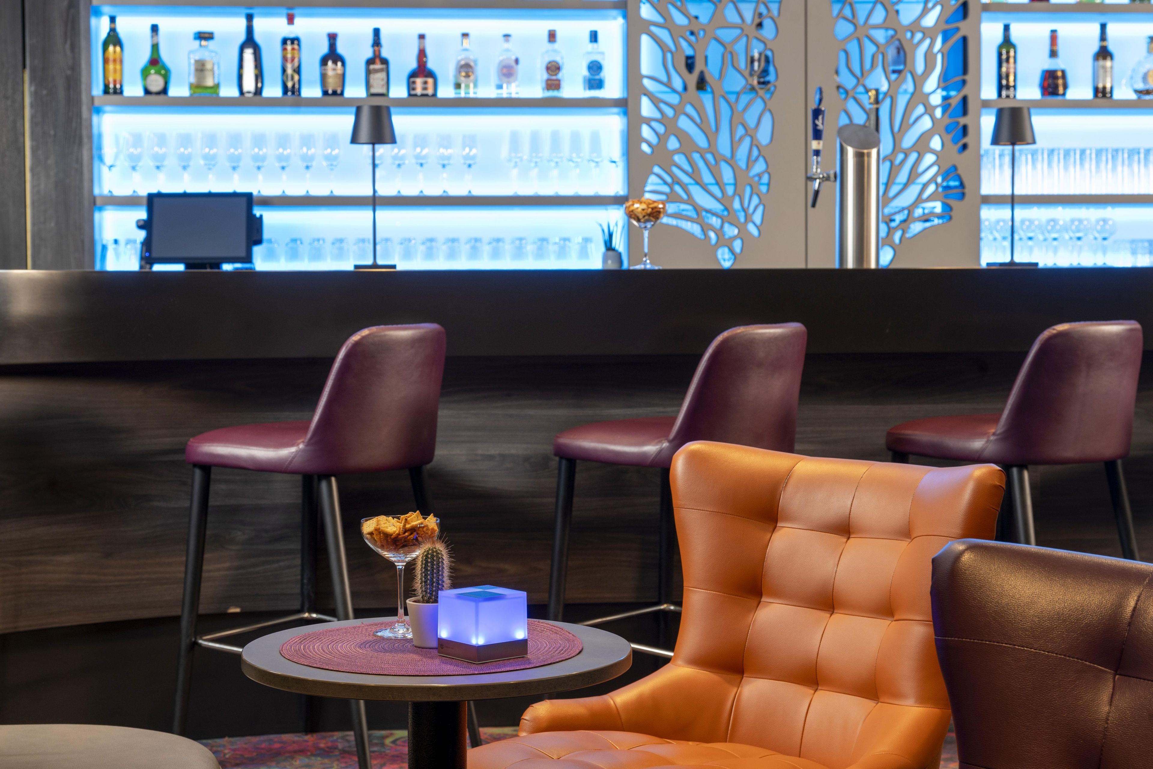 Un coin bar avec un assortiment de bouteilles, un cactus en guise de décoration centrale et des fauteuils en cuir.