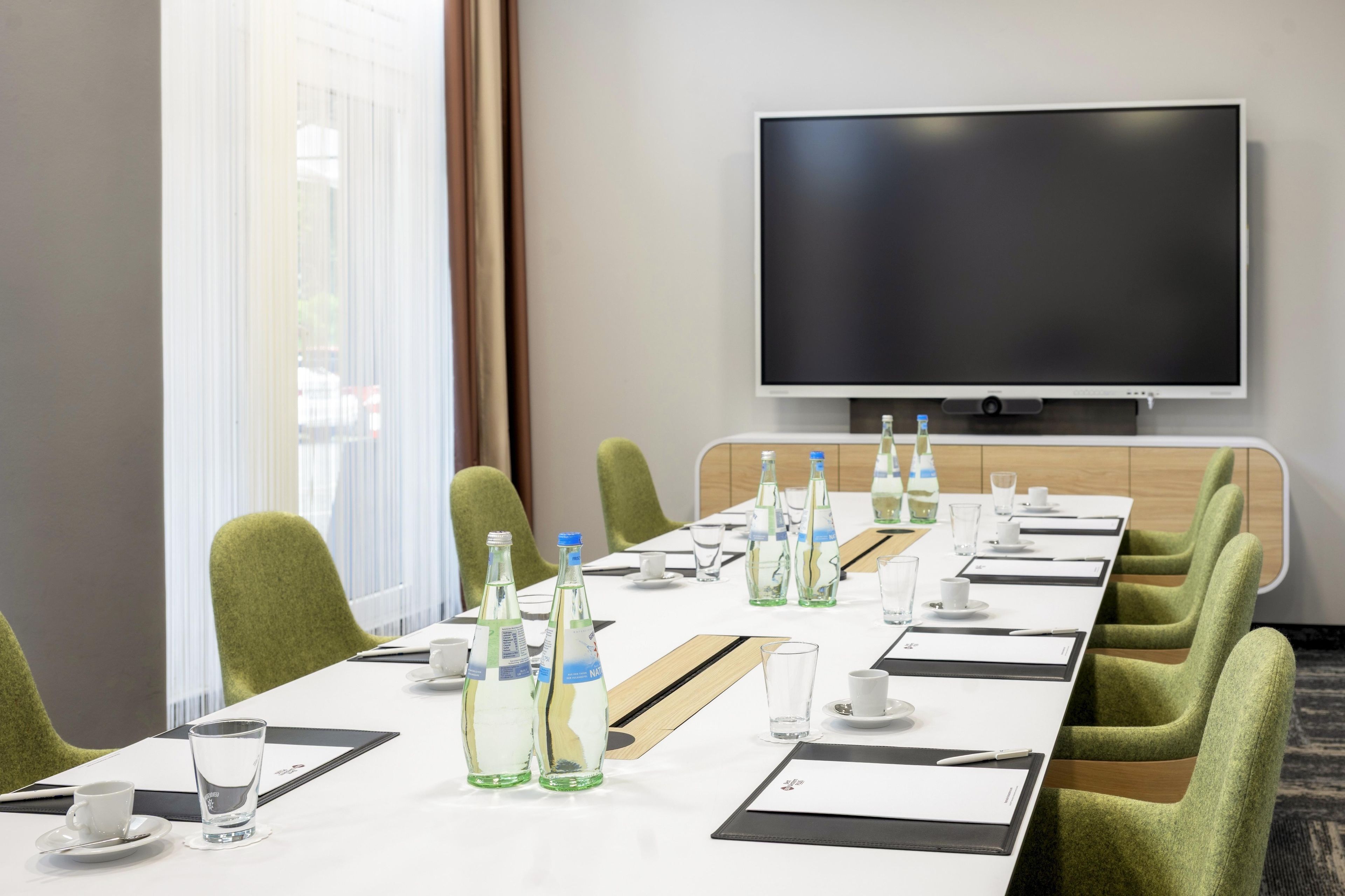 A conference room with a long table, chairs, a flat-screen TV, and water bottles.