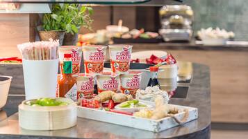 Una mesa de buffet con diferentes alimentos, incluyendo tazones de fideos, salsas y verduras.