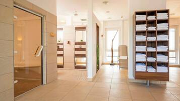 Welcome to our hotel lobby, featuring a reception area with a glass partition, a bench, and a shelf with neatly folded towels.