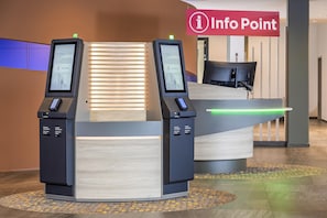 A reception desk with two self-service kiosks, a sign indicating an Info Point, and a modern interior design. - Best Western Plus Hotel Köln City (Cologne)