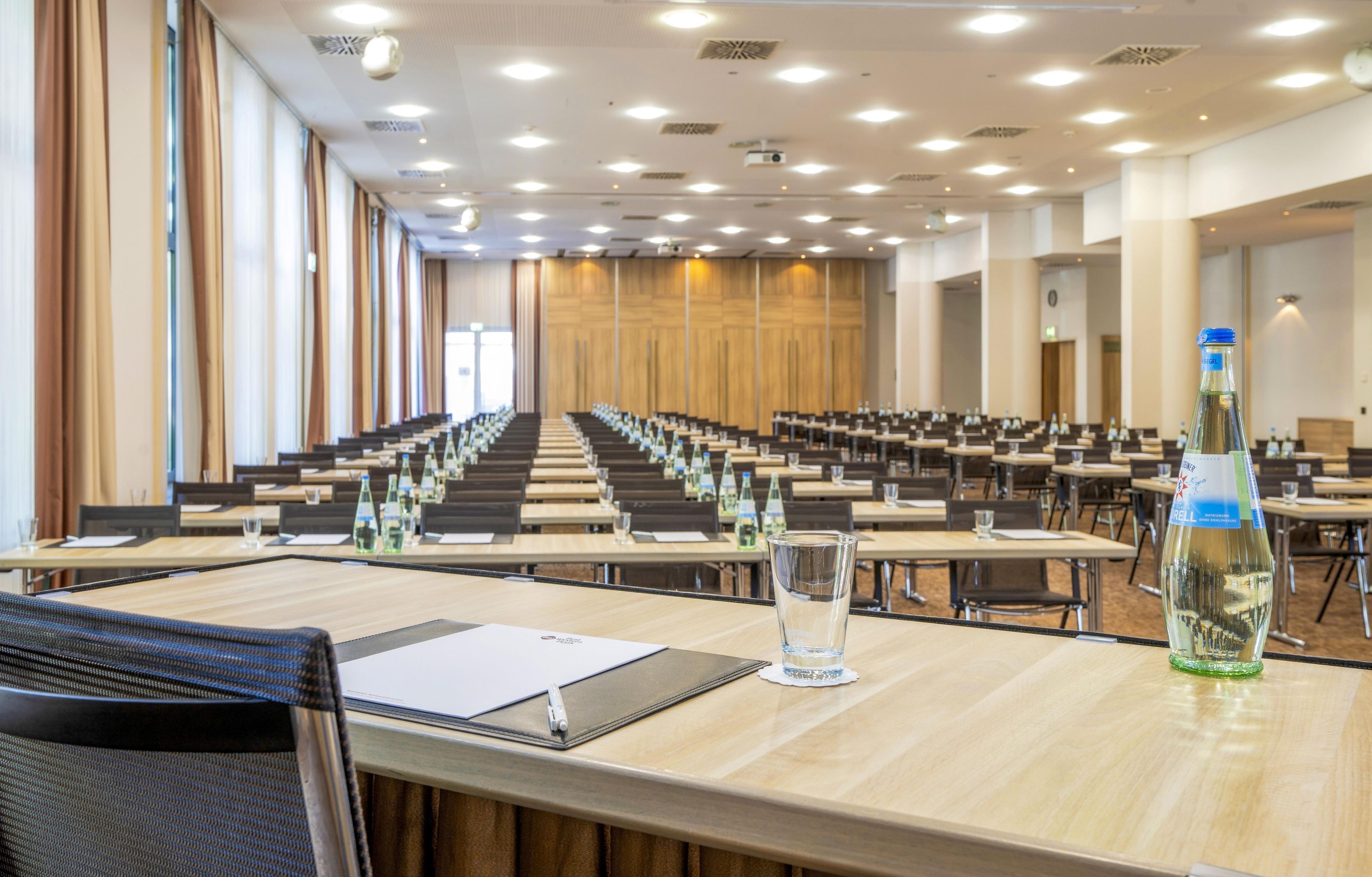 A conference room with rows of tables and chairs, equipped with water bottles and glasses.
