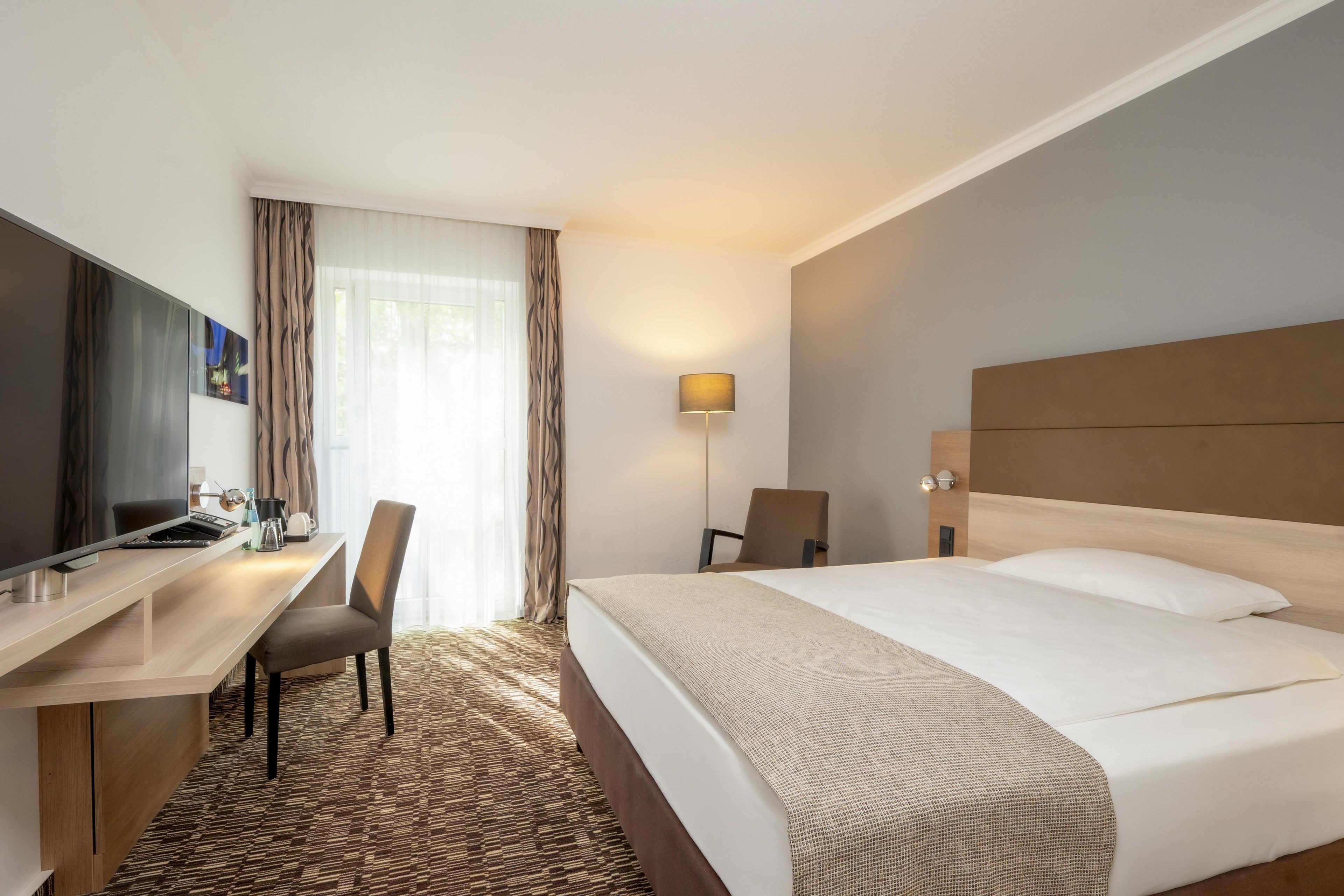 Una camera d'albergo con un letto, una scrivania, una sedia, una TV e una lampada.