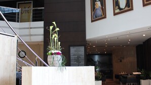 Eine moderne Lobby mit einer zentralen Treppe, einem Empfangstresen und gerahmten Portraits an den Wänden.