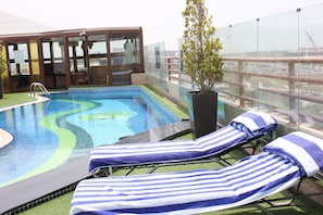Une piscine sur le toit, dotée de chaises longues et d’un espace clos par des parois de verre.