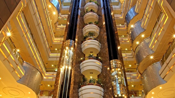 Ein mehrgeschossiges Atrium mit einer zentralen Treppe, mehreren Balkonen und einer hohen Decke mit Dachfenstern.