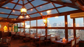 Ein Restaurant mit Glasdecke, Holzmöbeln und Blick auf die Stadt.