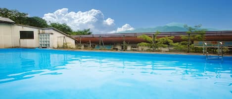 A swimming pool with a clear blue water surface, surrounded by a fence and a building with a flat roof.