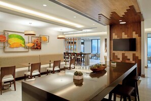 Un hall d’hôtel moderne avec un long bar, un espace salon et un téléviseur fixé au mur.