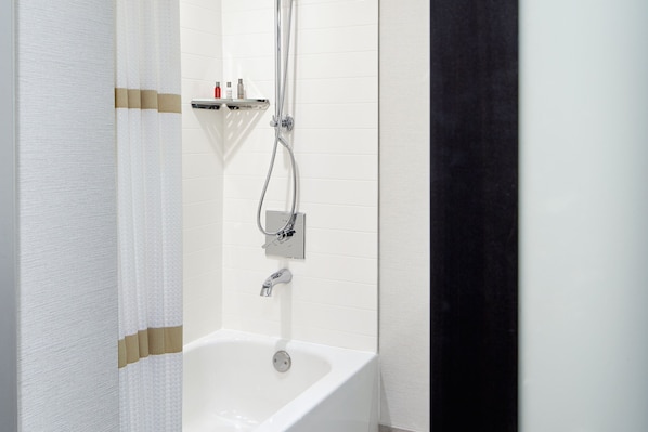Un baño moderno con una bañera blanca, ducha y estante con artículos de aseo.
