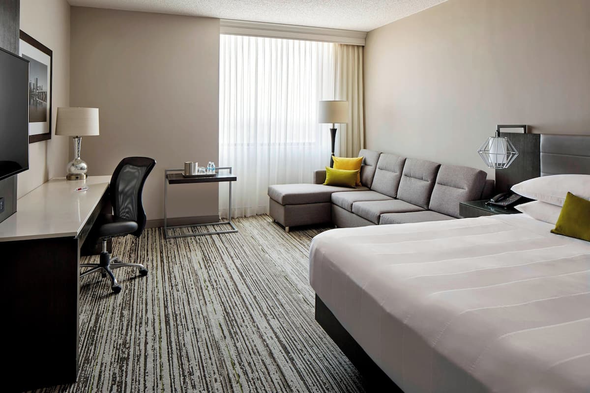 Une chambre d’hôtel avec un grand lit, un canapé, un bureau avec une chaise, une télévision et une fenêtre avec des rideaux.