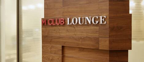 Pared de madera con el texto "M CLUB LOUNGE", indicando un área de lounge.