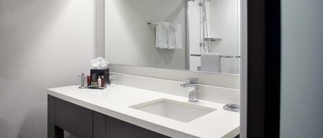 A modern bathroom with a white sink, a large mirror, and a shower visible in the reflection.