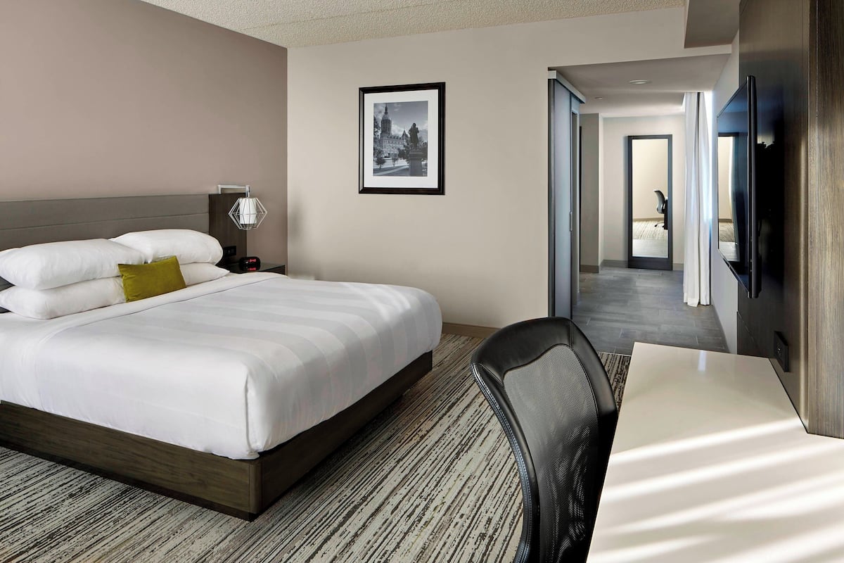 Une chambre d’hôtel avec un grand lit, un bureau, une chaise, un tableau encadré au mur et un téléviseur fixé au mur.