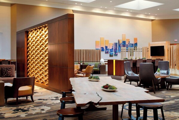 Un hall d’hôtel moderne avec un grand comptoir d’accueil en bois, des sièges confortables et une fresque murale représentant un paysage urbain.