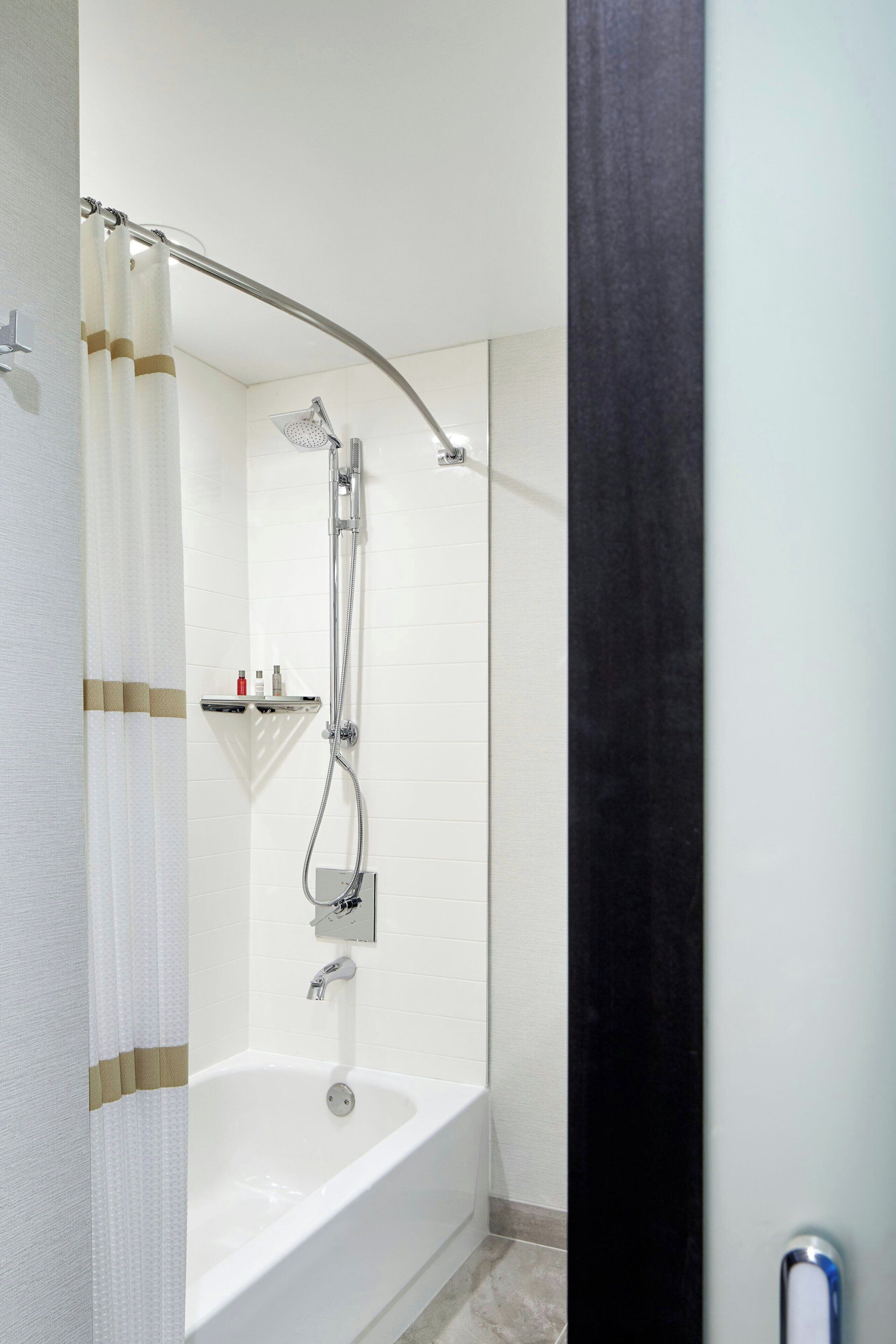 A modern bathroom with a bathtub, shower, and a shelf with toiletries.