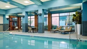 An indoor swimming pool with clear water, surrounded by lounge chairs and a table.