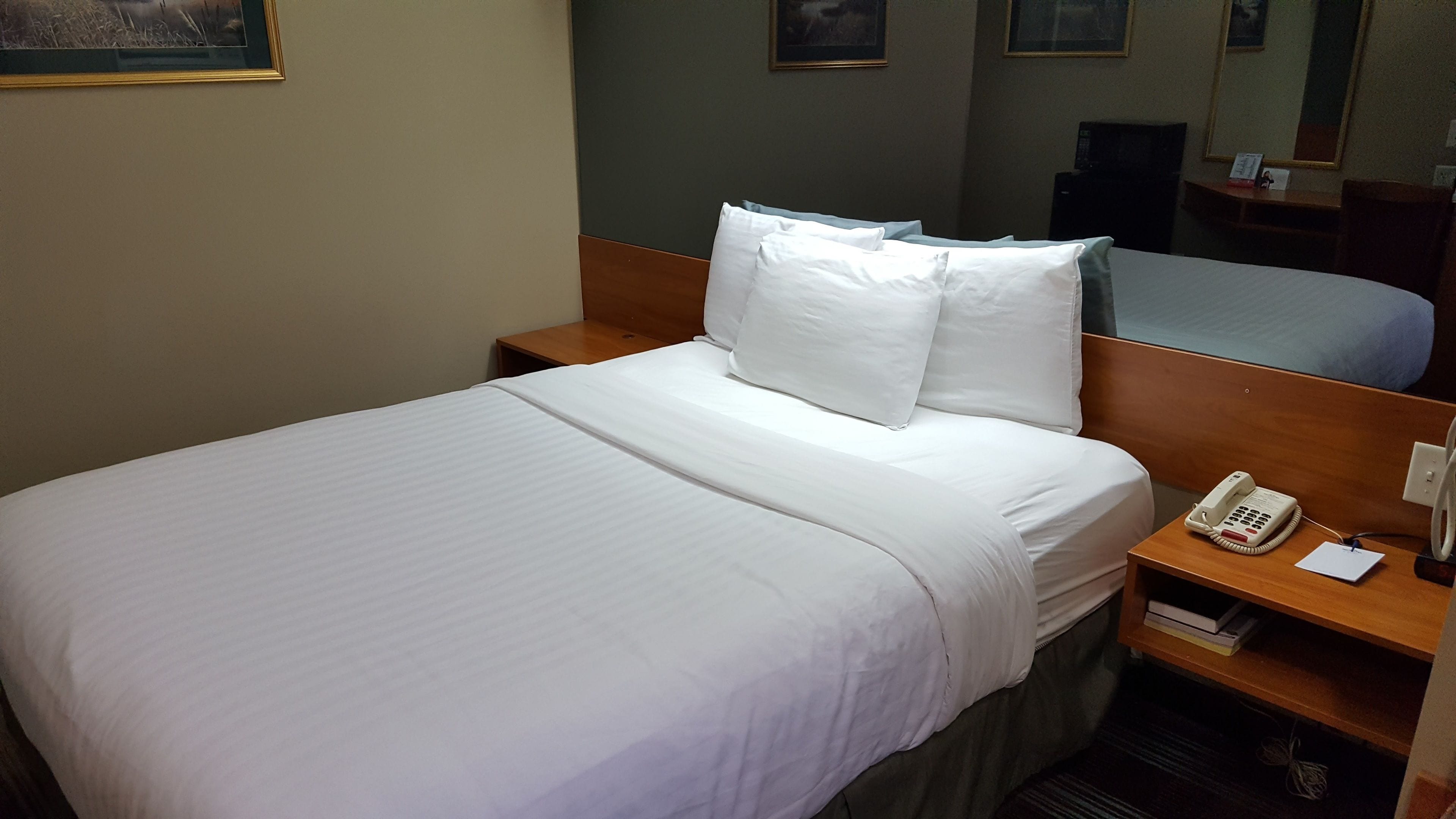 A hotel room with a neatly made bed, a bedside telephone, and a mirror on the wall.
