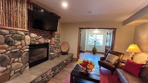 A stone fireplace with a flat-screen TV, a coffee table with a vase of flowers, a leather sofa, and a lamp. - Microtel Inn & Suites by Wyndham Bozeman (Bozeman)
