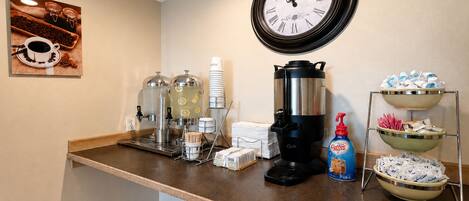 A coffee station with a coffee maker, cups, and a coffee dispenser.