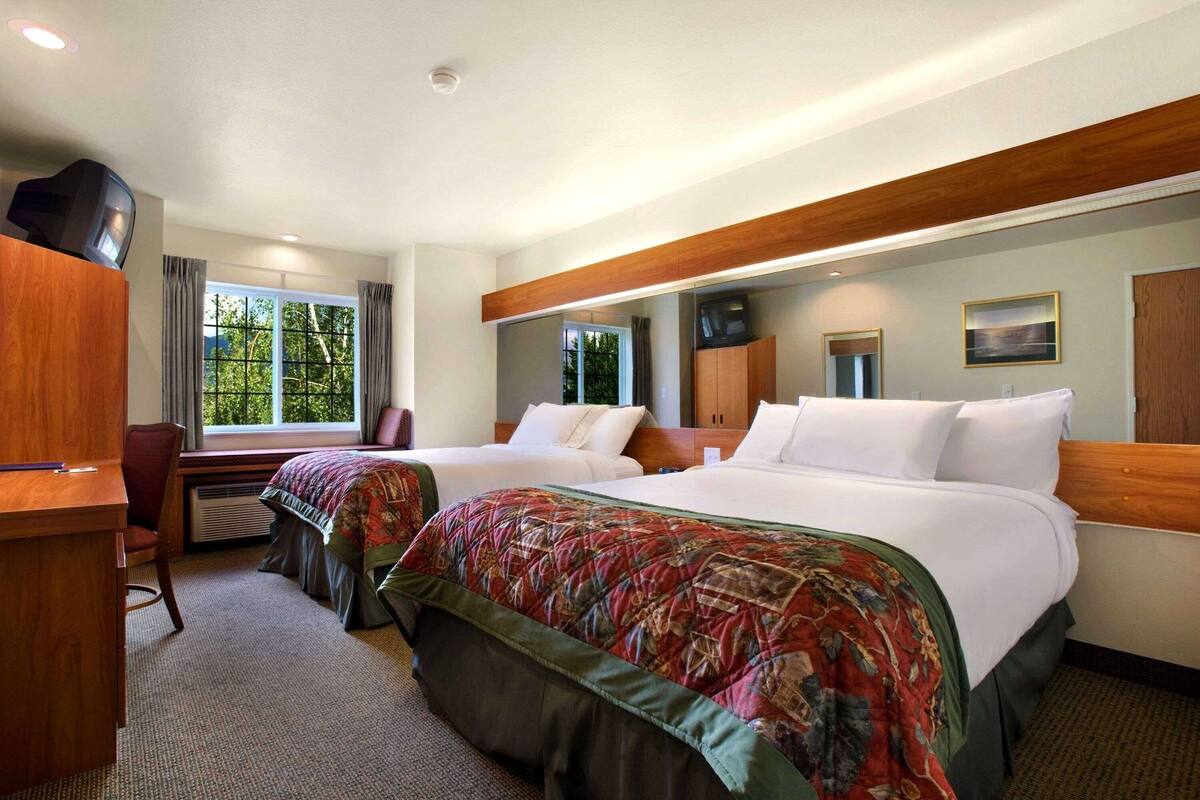 Une chambre d’hôtel avec deux lits, un bureau, une chaise et un téléviseur.