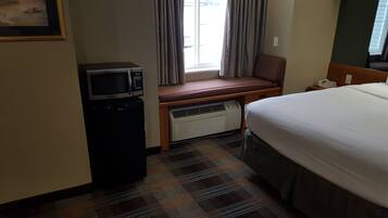 A hotel room with a bed, a desk with a chair, a microwave, and a heater.