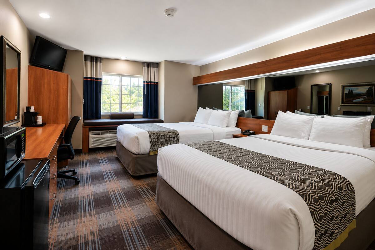 Une chambre d’hôtel avec deux lits, un bureau avec un ordinateur, une télévision et une fenêtre avec des rideaux.
