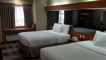 Een hotelkamer met twee bedden, een raam met gordijnen, een nachtkastje met een telefoon en een grote spiegel.